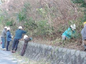 石積みに沿って外から笹刈り作業をする参加者と子ども