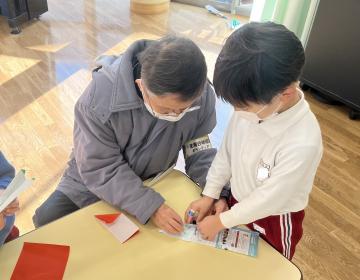 紙飛行機の折り方を教えてもらっている