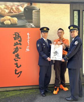 高山製菓の前で警察署長、高山製菓株式会社代表取締役、生駒市消防長が一緒に完成した袋を持っています
